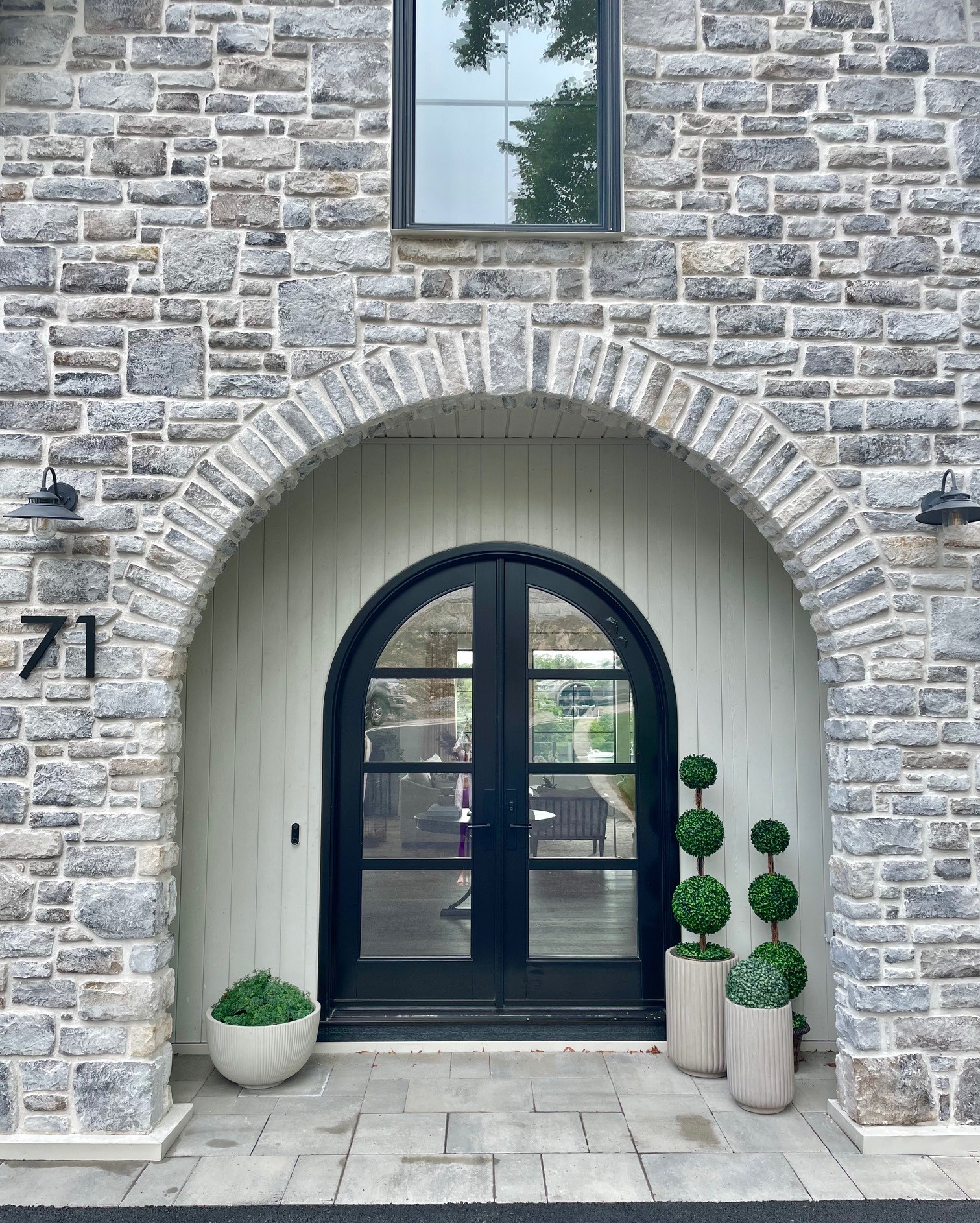 A stunning stone arch and thoughtfully placed greenery and topiaries greets guests as they enter the home
